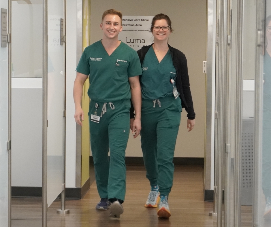 A Man and woman in green scrubs walking down a clinical hallway